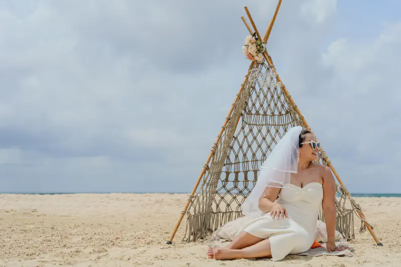 Bride-to-be posing by macramé teepee on beach