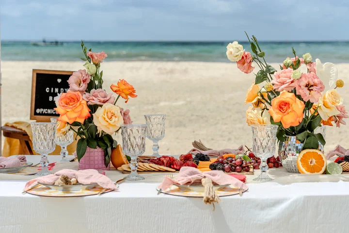 Orange and pink roses, crystal glasses and charcuterie on a beach picnic table