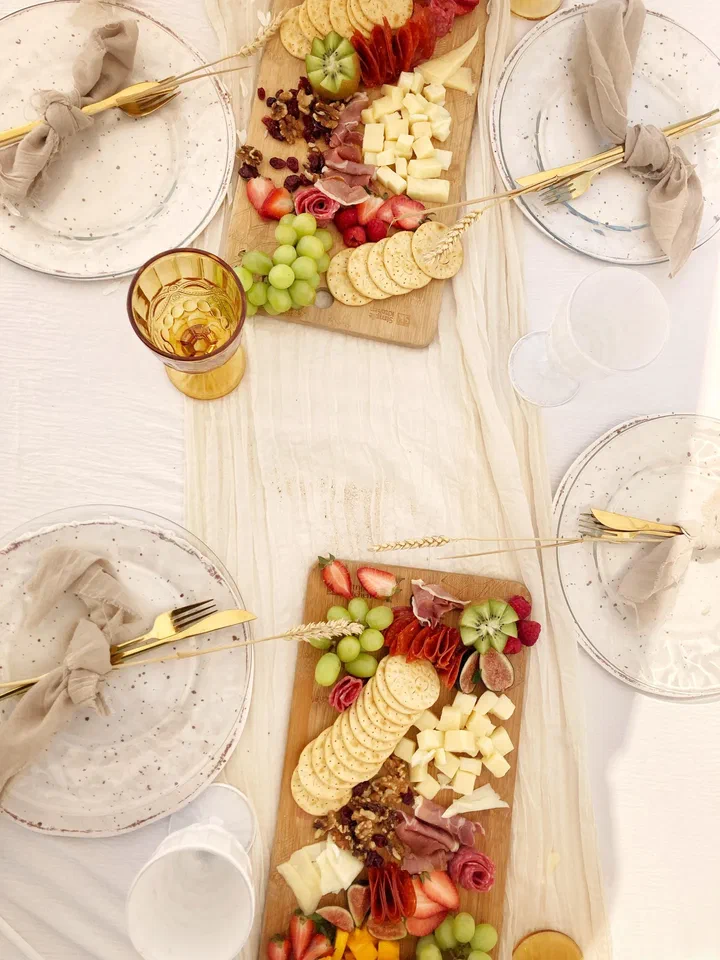 Overhead view of two charcuterie boards with fruit, gold cutlery and linen napkins