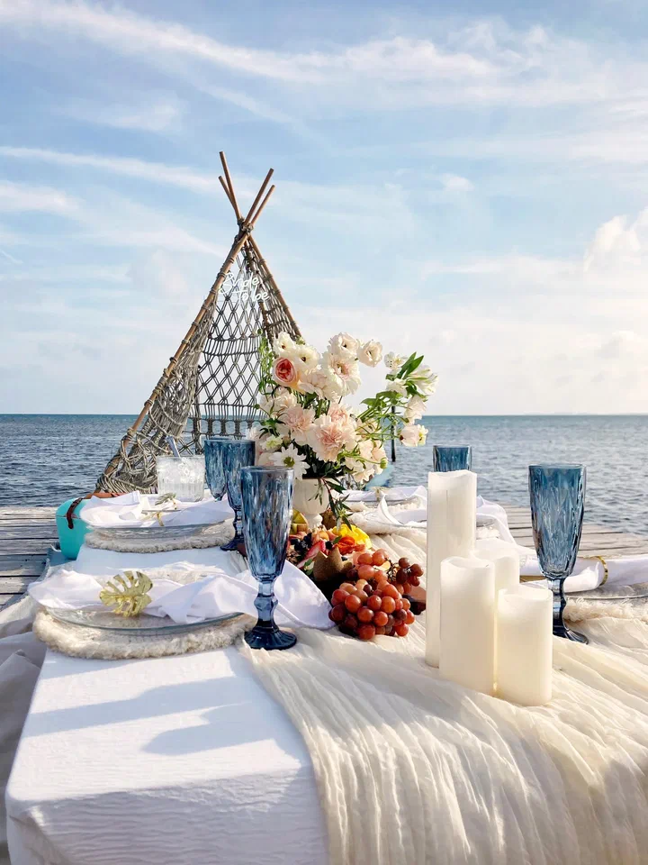 Candles, blue glassware and charcuterie under a teepee on a dock by the sea