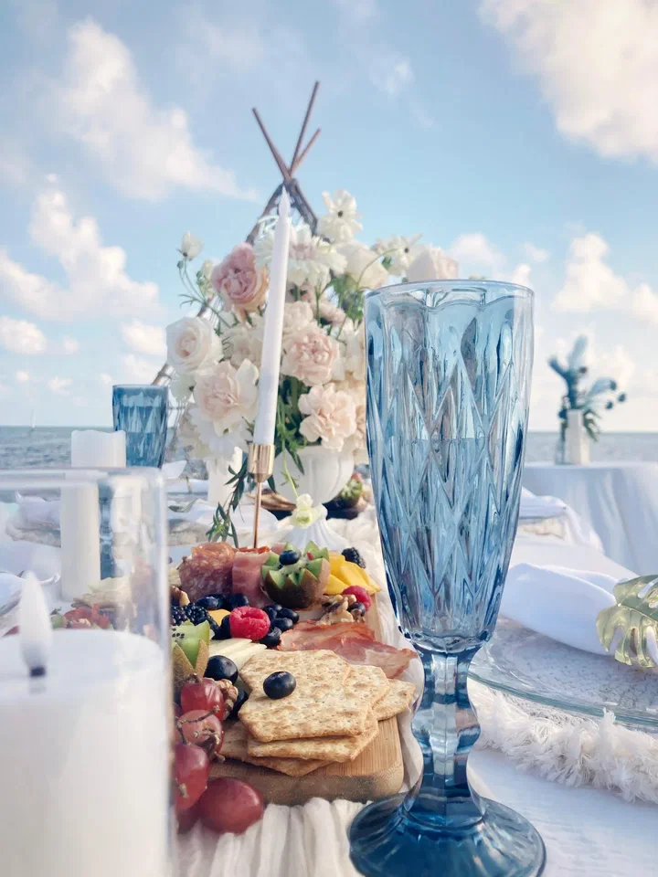 Blue crystal glass beside candles, a charcuterie board and white flowers