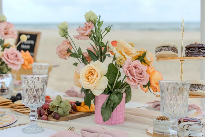 Pink and peach flowers with crystal glasses and charcuterie on a beach picnic table