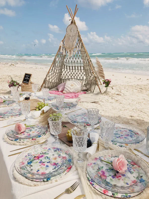 Montaje de picnic junto al mar con platos florales y teepee de macramé