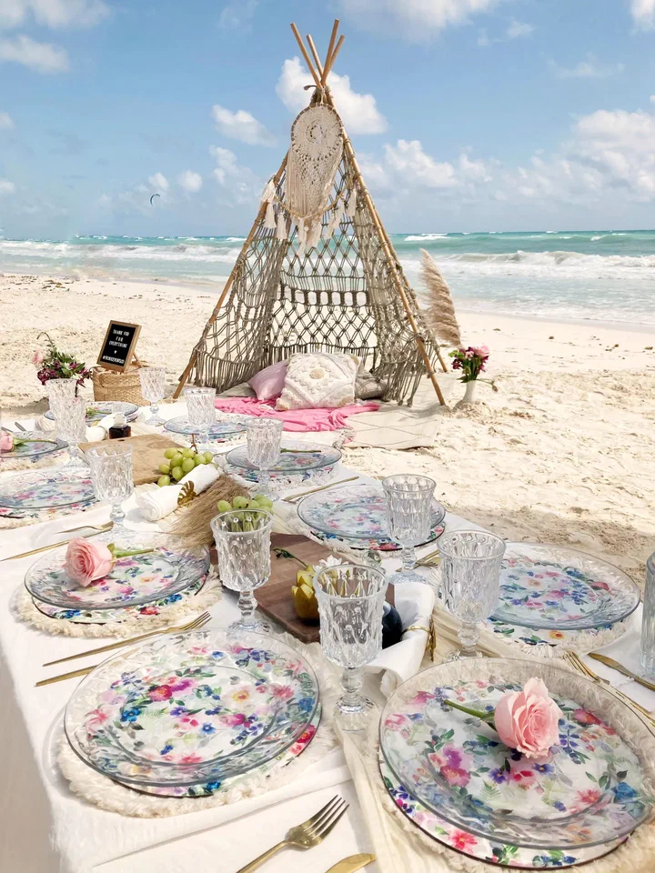 Beach picnic with floral glass plates, a pink rose and a macramé teepee by the sea