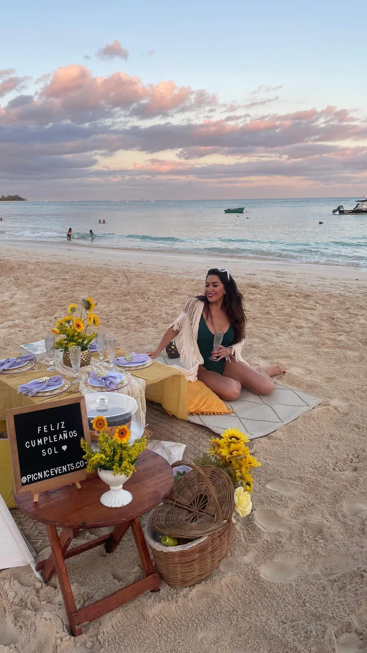 Woman sitting beside a sunflower birthday picnic on the beach at sunset