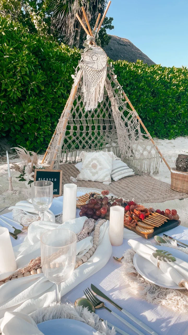 Macramé teepee against a green hedge above a table of charcuterie, candles and white linen