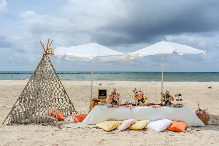 Macramé teepee picnic with white umbrellas and floor cushions on a Riviera Maya beach