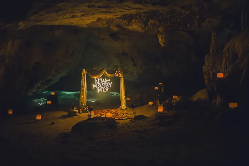 Romantic cave proposal scene with illuminated &lsquo;marry me&rsquo; sign