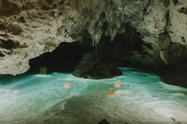 Vista cercana de una piscina de agua turquesa dentro de un cenote, rodeada de formaciones rocosas naturales e iluminación ambiental suave