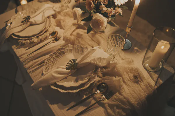 Primer plano de una mesa refinada con platos en capas, copas de cristal y servilletas adornadas con motivos de hojas metálicas