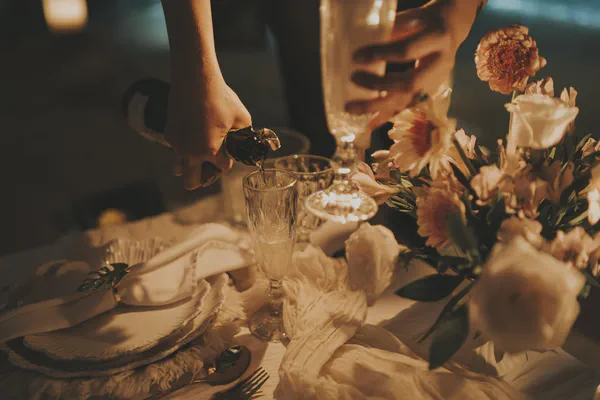 Primer plano de una botella de champagne siendo servida en copas de cristal, con un arreglo floral de flores color durazno y rosa pálido