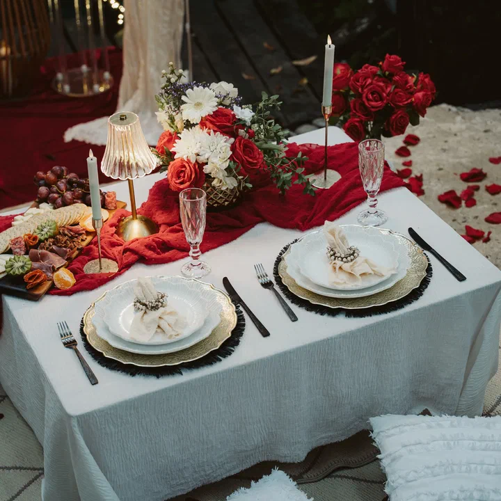 A candlelit table for two with red roses, a grazing board and champagne flutes.