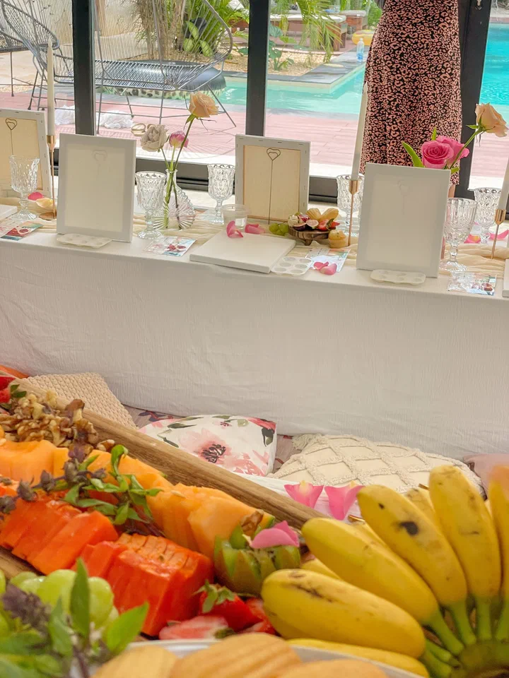 Papaya, bananas and other tropical fruit on a platter in front of a painting table set with blank canvases.