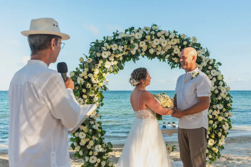 Romantic beach ceremony with white floral arch and ocean backdrop