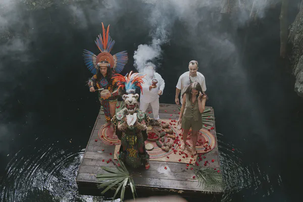 Overhead view of a traditional Mayan ceremony on a platform suspended over crystal clear cenote waters
