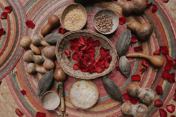 Mazorcas de cacao, jícaras, granos de maíz y una canasta de pétalos de rosa roja sobre un petate para una ceremonia maya.