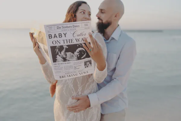 Expectant couple holding a baby-on-the-way newspaper during a pregnancy announcement photoshoot in Playa del Carmen