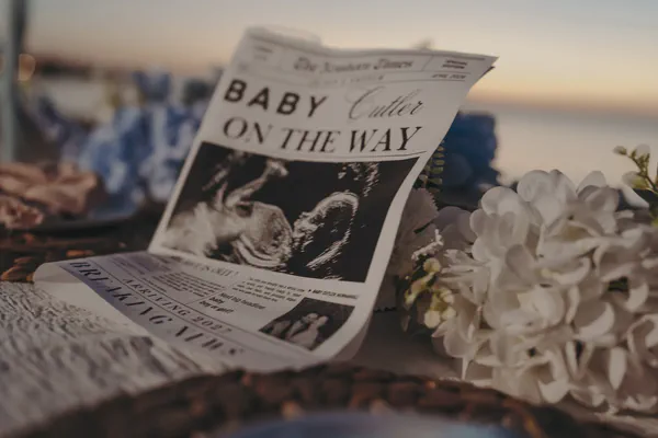 Baby announcement newspaper displayed beside flowers and cake on the picnic table