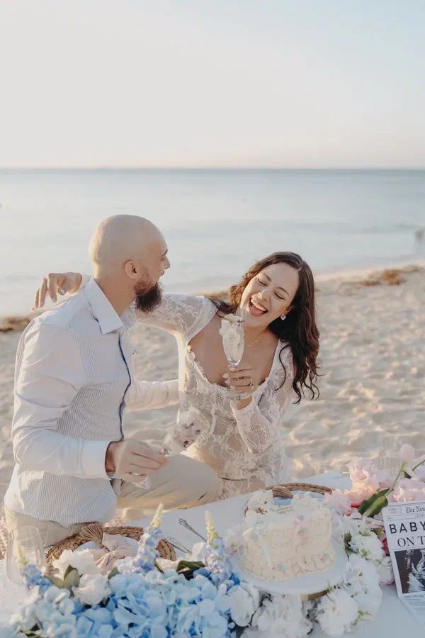 Parents-to-be laughing over cake and flowers after their Riviera Maya beach gender reveal