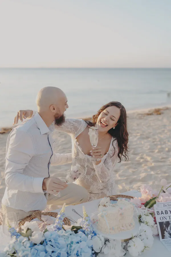 Parents-to-be laughing over cake and flowers after their Riviera Maya beach gender reveal