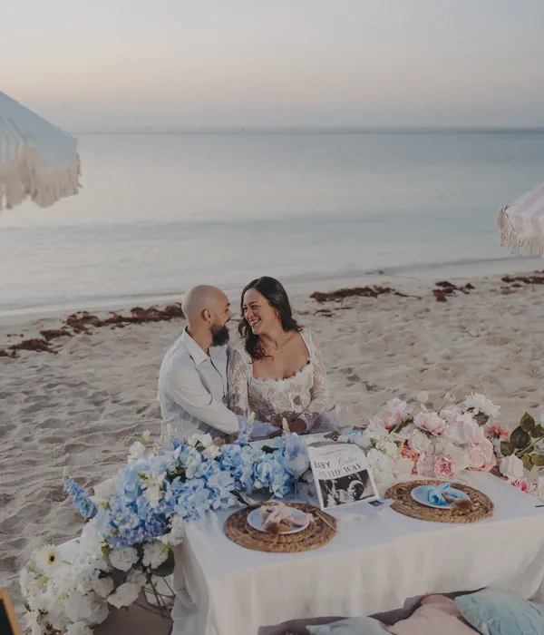 Expectant couple seated at their decorated picnic table on the beach in Riviera Maya