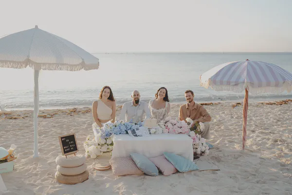 Wide sunrise view of four guests gathered around a decorated beach picnic in Riviera Maya