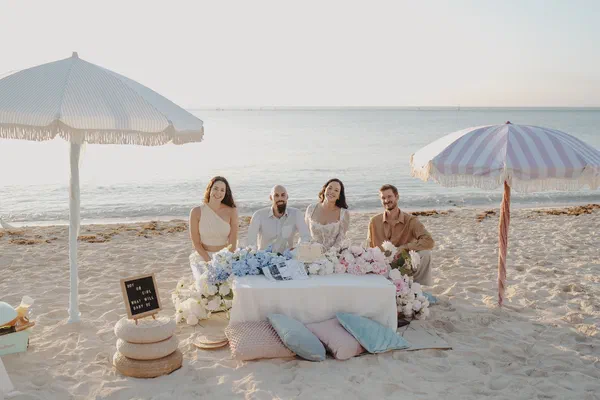 Wide sunrise view of four guests gathered around a decorated beach picnic in Riviera Maya