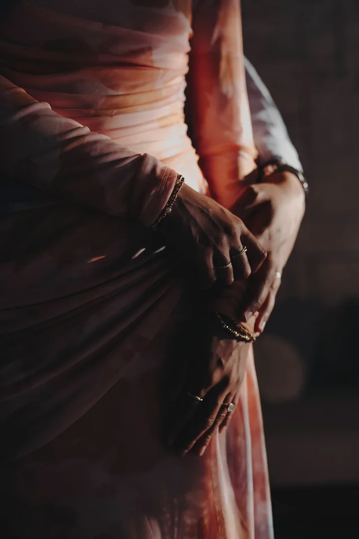 Close-up of a couple’s hands resting together over a rose-colored dress