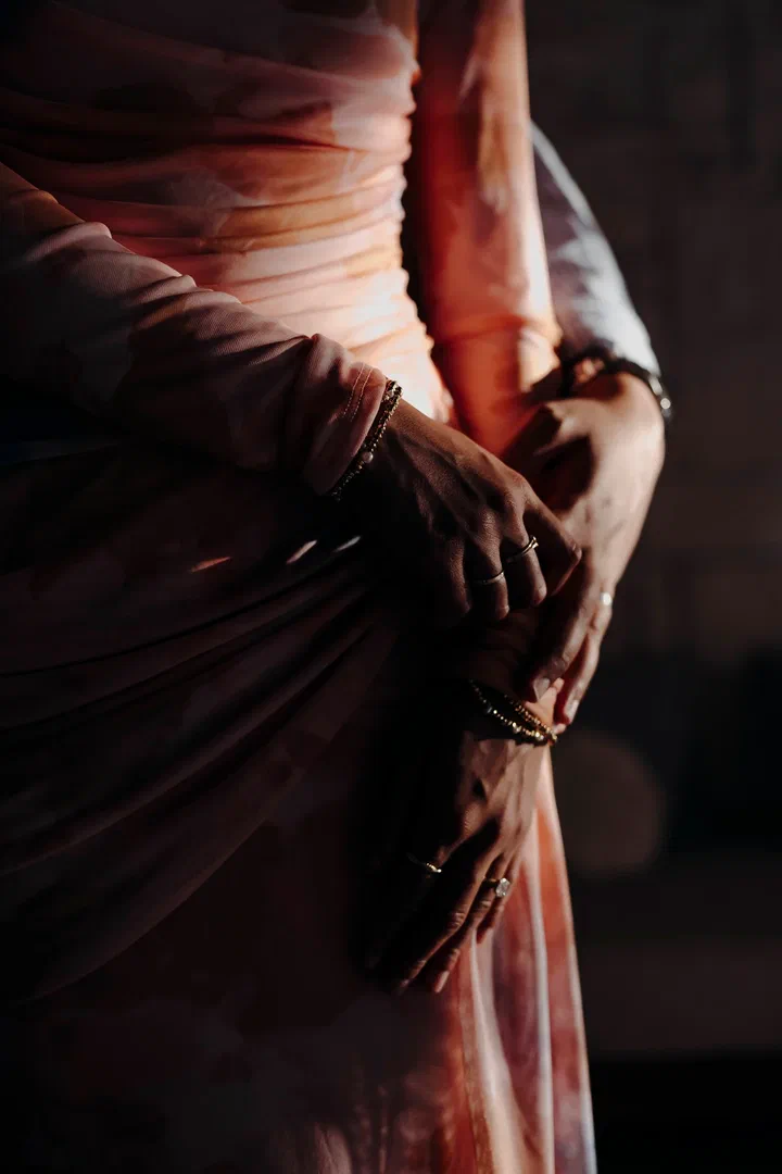 Close-up of a couple’s hands resting together over a rose-colored dress