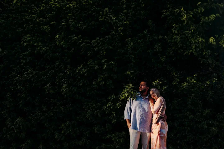 Couple standing close together against a wide backdrop of dark green foliage