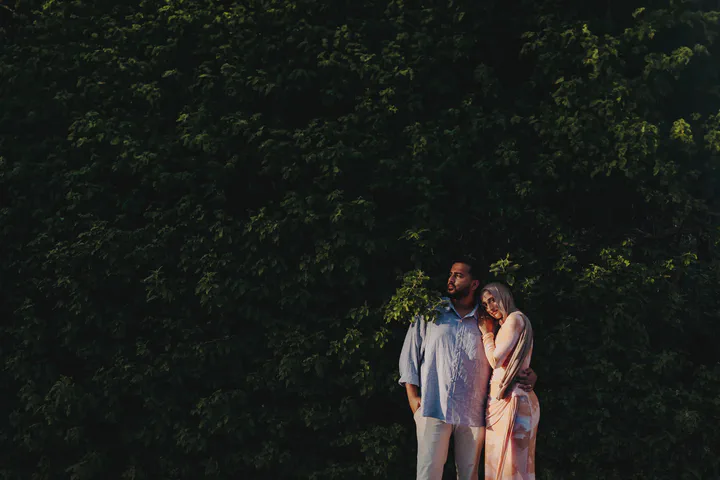 Couple standing close together against a wide backdrop of dark green foliage