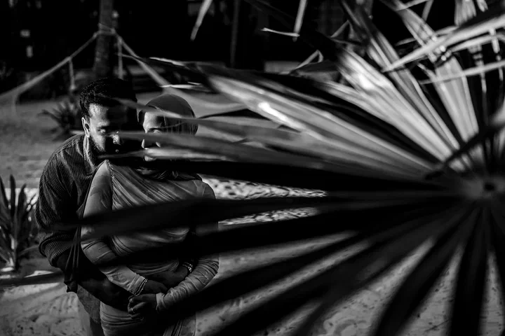 Black-and-white portrait of a couple partly hidden by a large palm frond