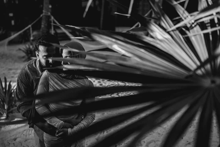 Black-and-white portrait of a couple partly hidden by a large palm frond
