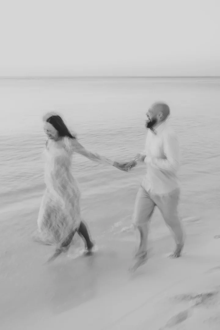 Black-and-white motion-blurred photograph of a couple holding hands by the sea