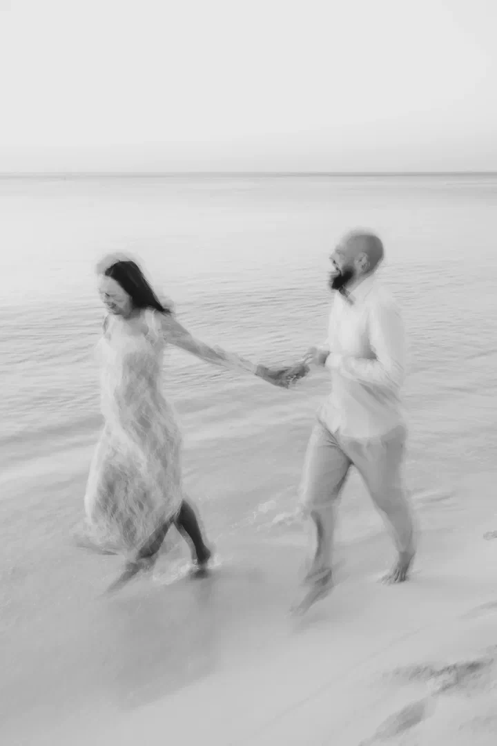 Black-and-white motion-blurred photograph of a couple holding hands by the sea