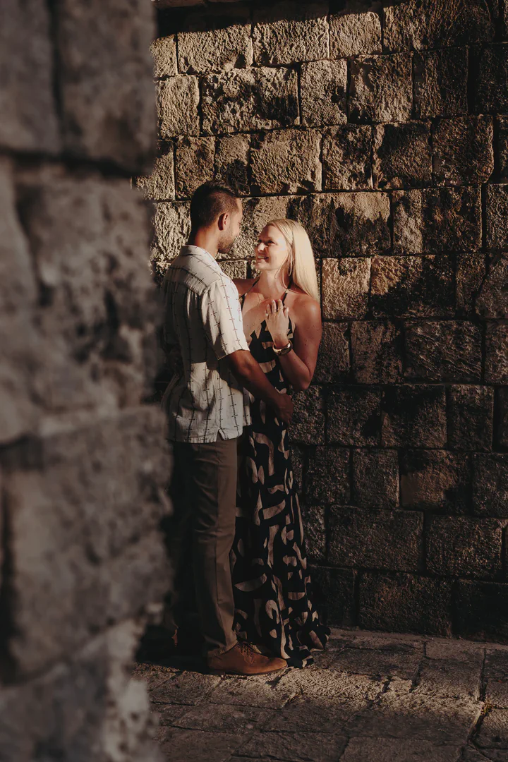 Couple holding each other in a sunlit opening between stone walls