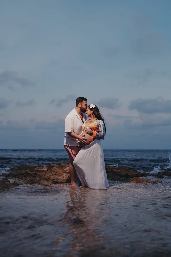 Expectant couple embracing in shallow water at twilight