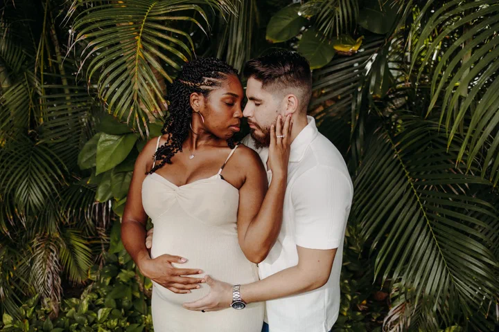 Expectant couple touching foreheads in front of dense tropical palms