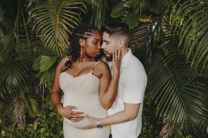 Expectant couple touching foreheads in front of dense tropical palms