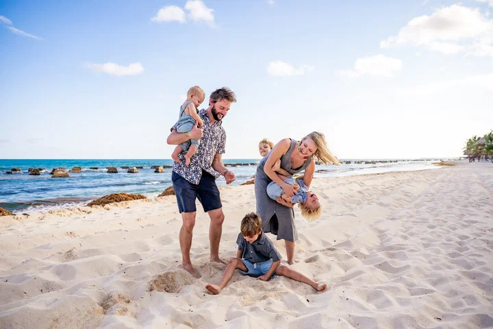 Family of five playing on the beach, with children on their parents’ shoulders