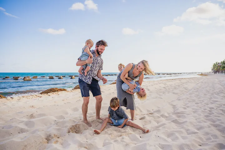 Family of five playing on the beach, with children on their parents’ shoulders