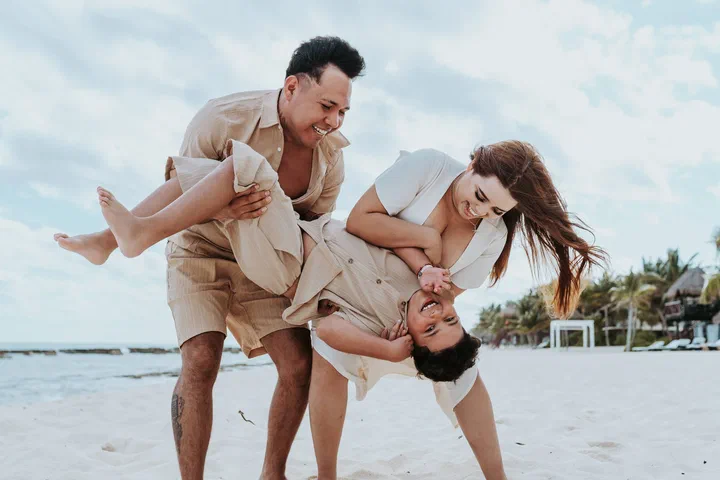 Parents laughing as they hold their children upside down on the beach