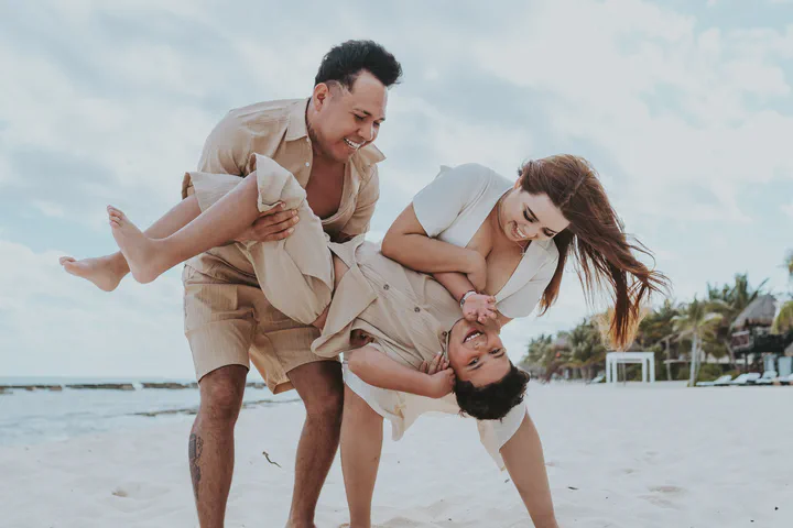 Parents laughing as they hold their children upside down on the beach