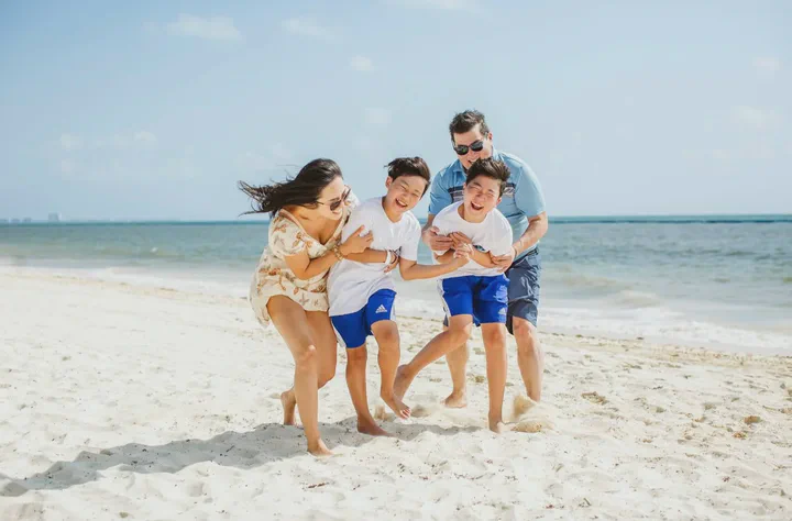 Family of four laughing and running together across white sand