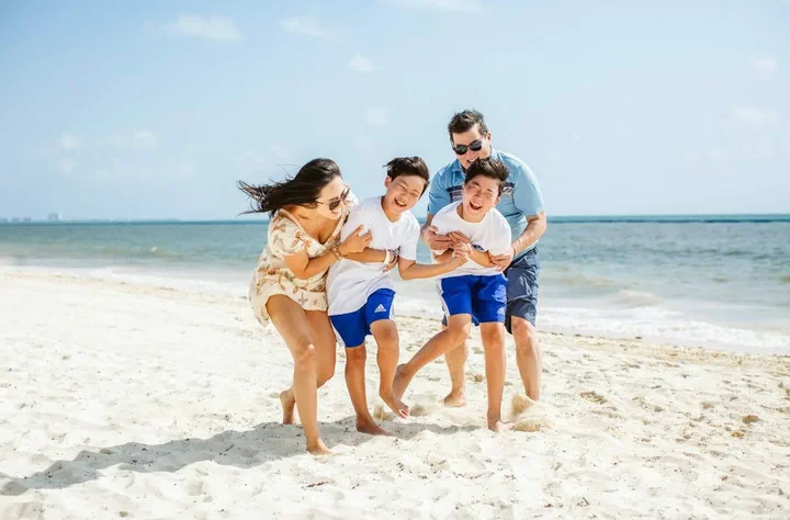 Family of four laughing and running together across white sand