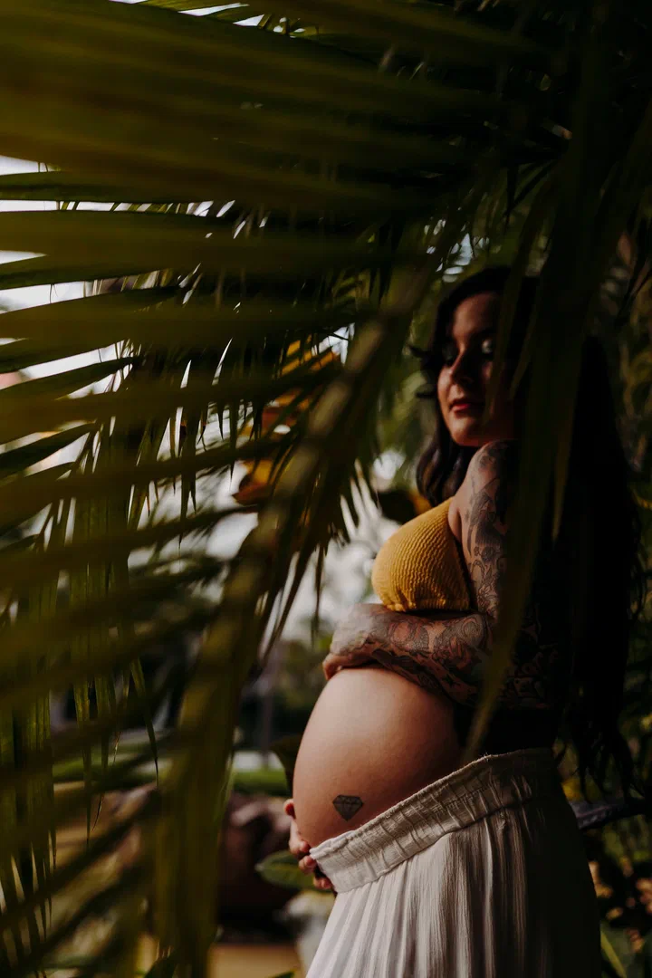 Expectant mother framed by palm leaves and dappled sunlight