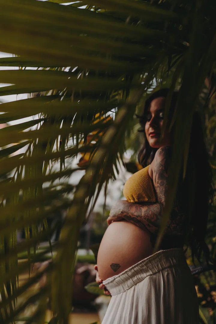 Expectant mother framed by palm leaves and dappled sunlight