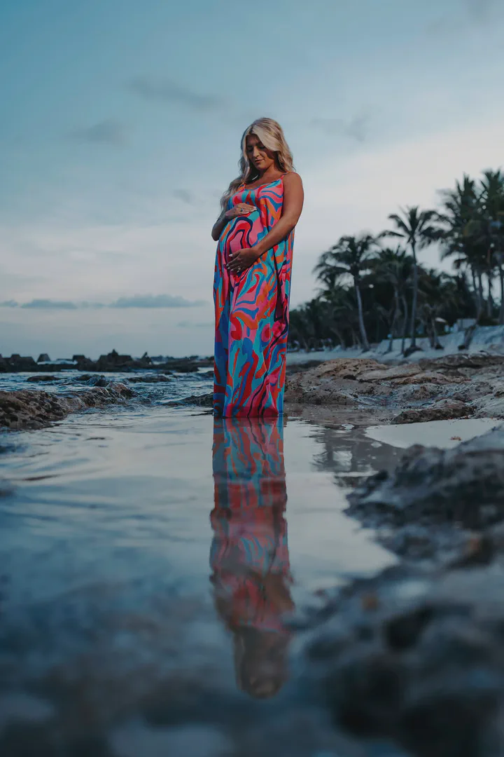 Expectant mother in a colorful dress reflected in a coastal tide pool