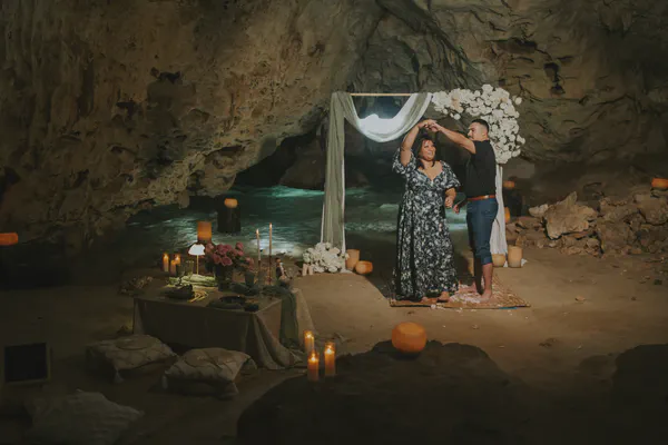 Espacio íntimo en el legendario Cenote Ik Kil, donde aguas turquesas y formaciones de piedra caliza crean un ambiente mágico; un arco de tela blanca con arreglos florales y una mesa decorada con velas y flores establecen el escenario perfecto para el momento especial.