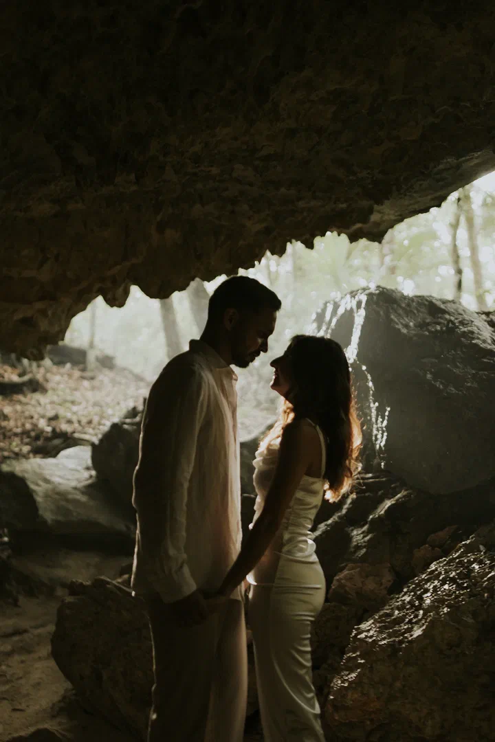 Pareja frente a frente en la entrada de un cenote, iluminada a contraluz